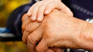 Nahaufnahme zweier Hände, eine ältere und eine jüngere, die sich miteinander halten. Hintergrund unscharf.
